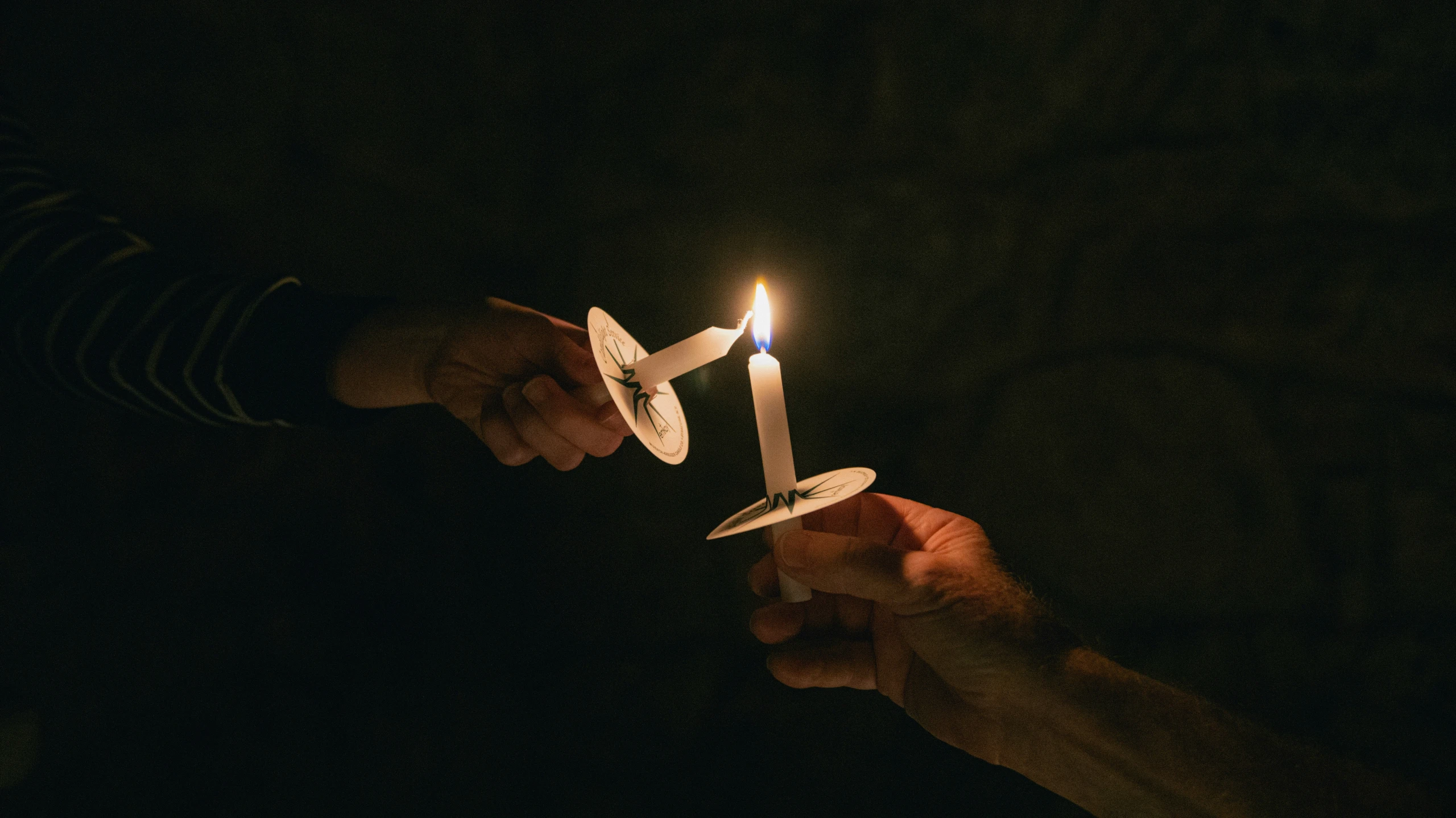 two hands holding a small lit candle in the dark