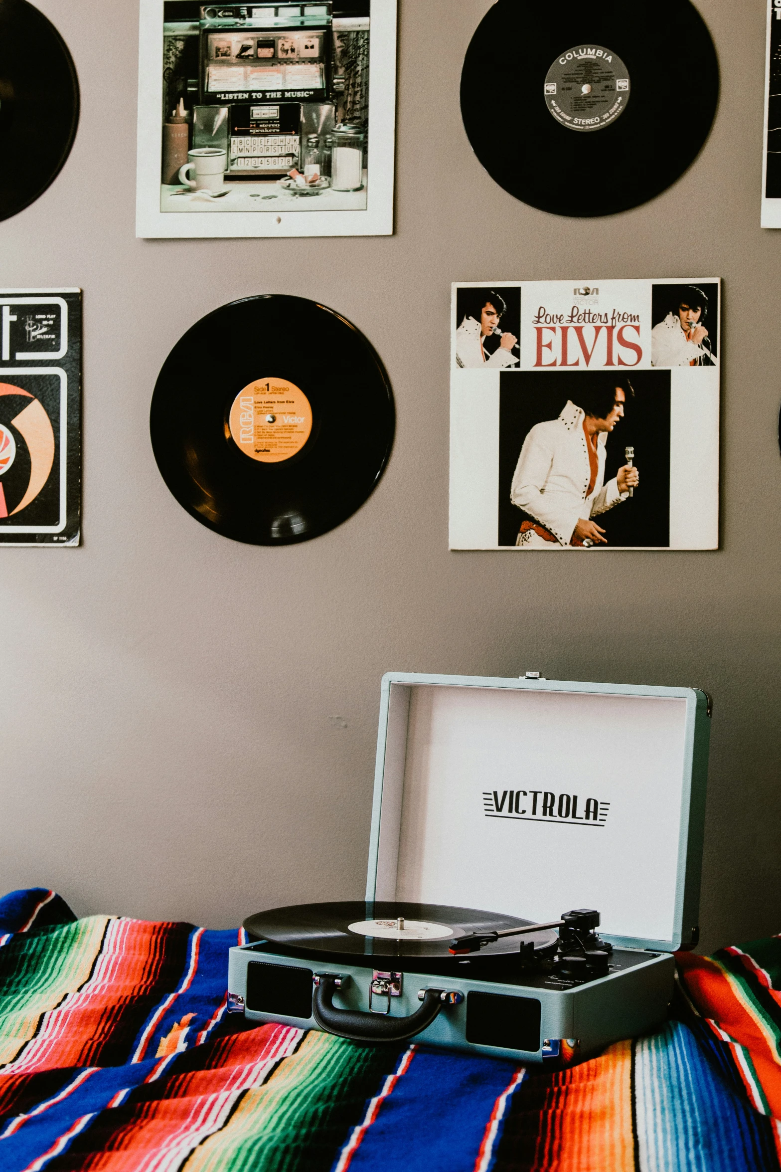 a bed topped with a suitcase and wall with lots of records