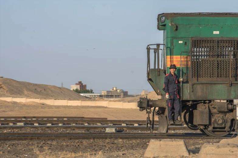 a man standing on top of train tracks near dirt hill