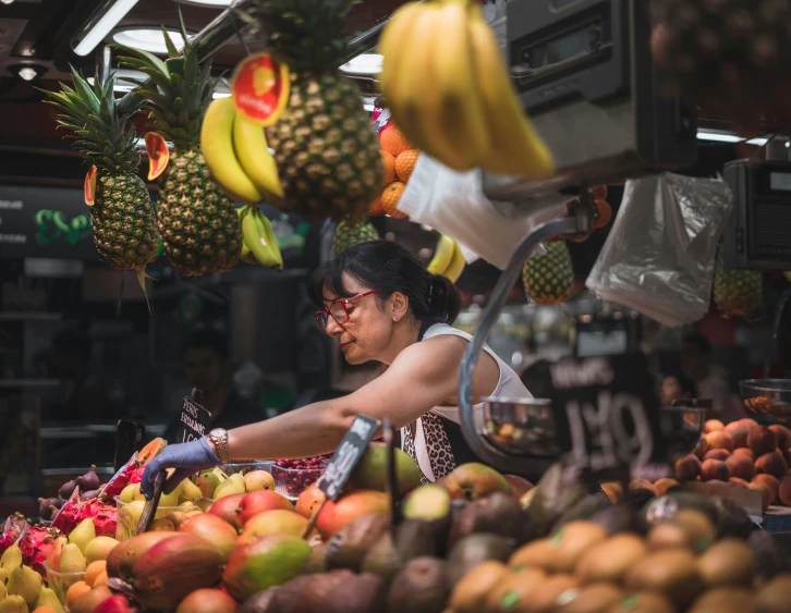 a woman reaching for fruit at a fruit stand