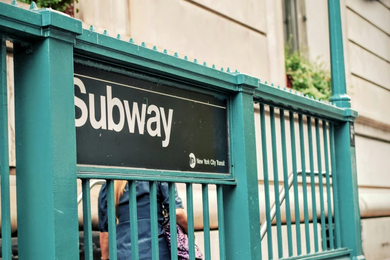 the sign for subway is attached to the green railing
