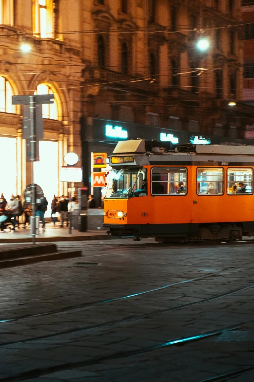 orange trolley car on tracks in city street