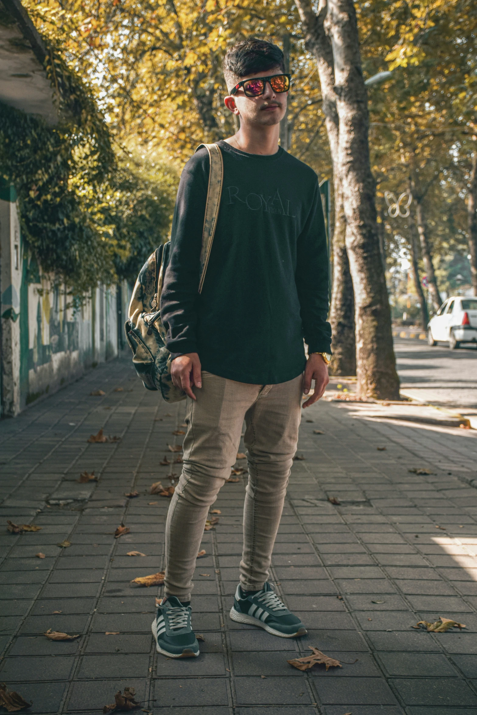 man in sunglasses and shirt standing on brick pavement next to trees