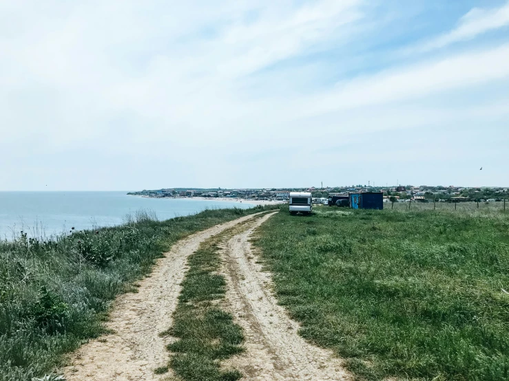 two vehicles are traveling down a dirt road by the water