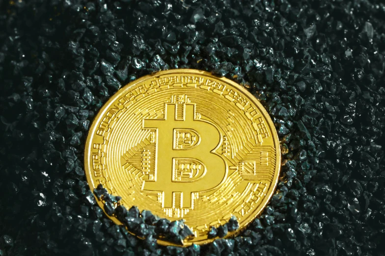 a gold bit coin in the middle of a pile of black plastic