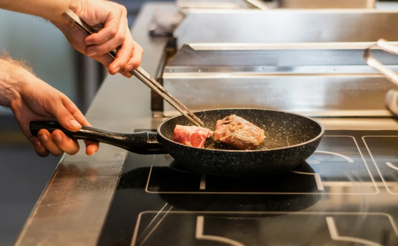 a chef uses a pair of tongs to stir beef in a set