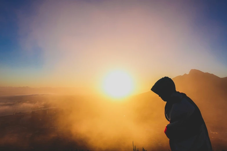 a person looking out into the sunset on a mountain