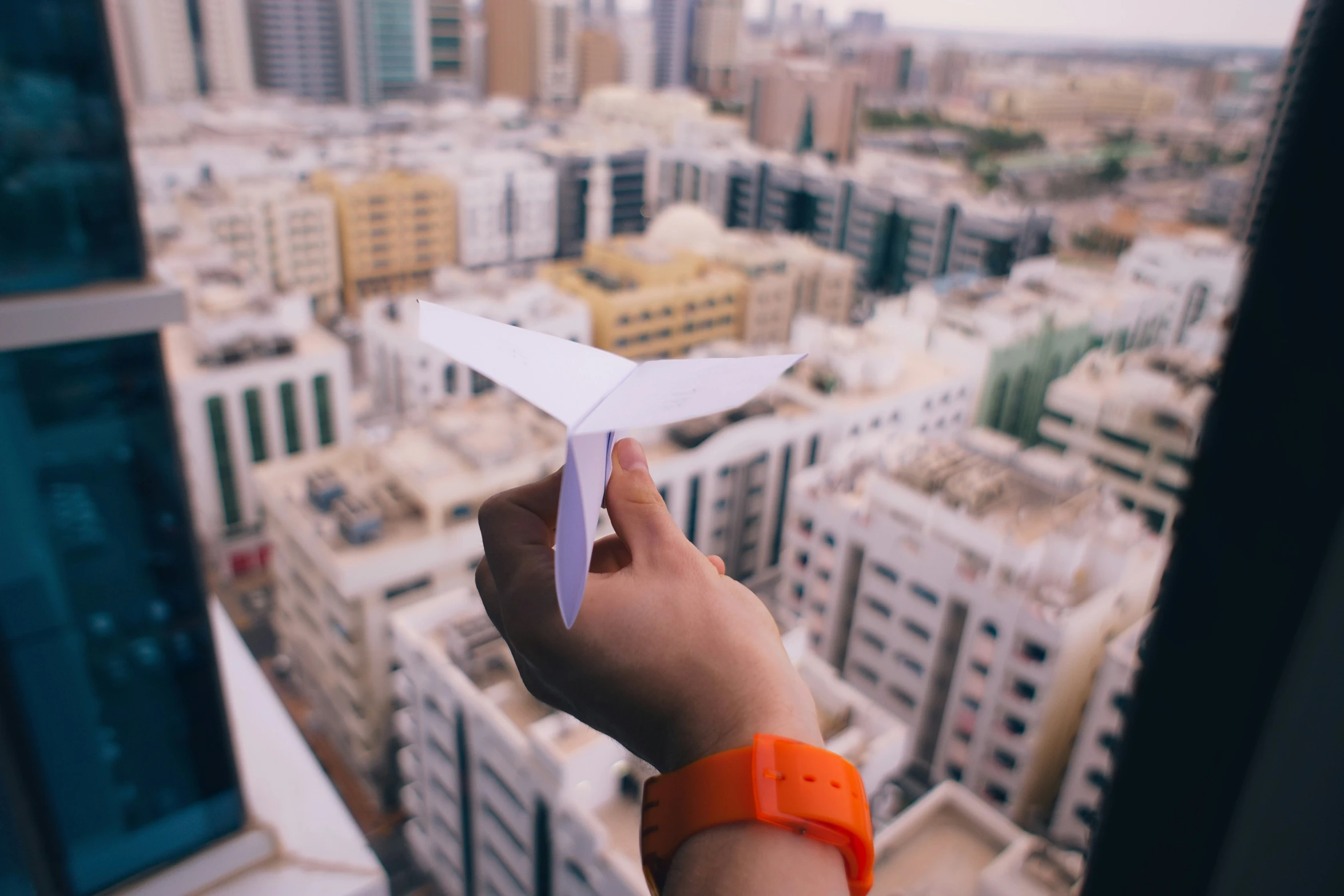 a person holds a small airplane that they are flying in front of a cityscape