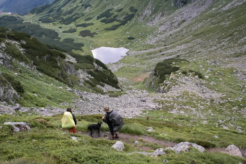 two people walk up a steep mountain while a dog sits by