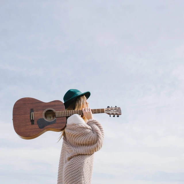 a  with a hat on standing next to an acoustic guitar