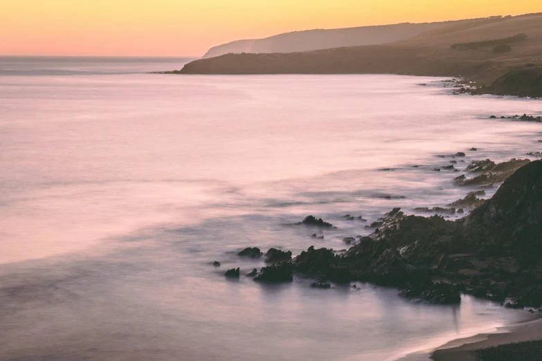 view of the water along a cliff shore during sunset