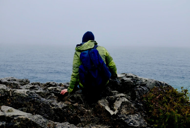 the man is sitting on the rocks near the water