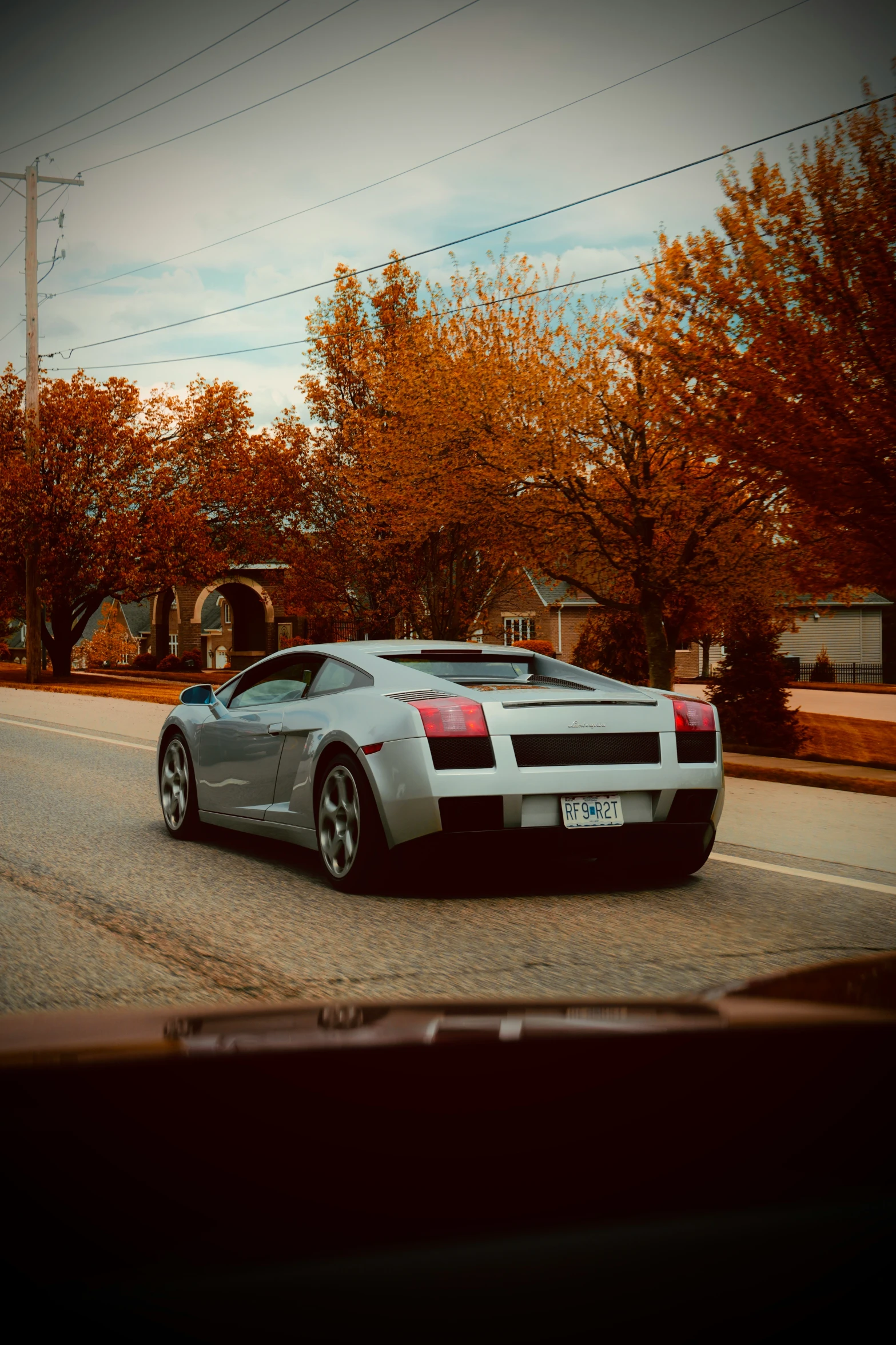 an automobile is moving down the road with autumn trees in the background