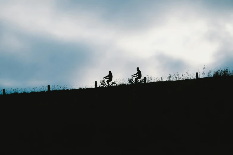 silhouettes of three men riding bicycles on a grassy hillside