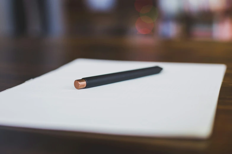 a pen and paper with pencil on a wooden table