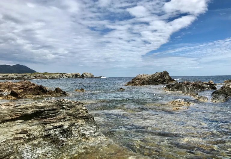 a rocky shoreline with clear water and cloudy sky