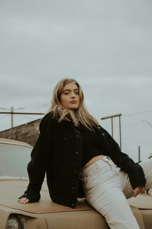 a beautiful blond haired woman posing on top of a car