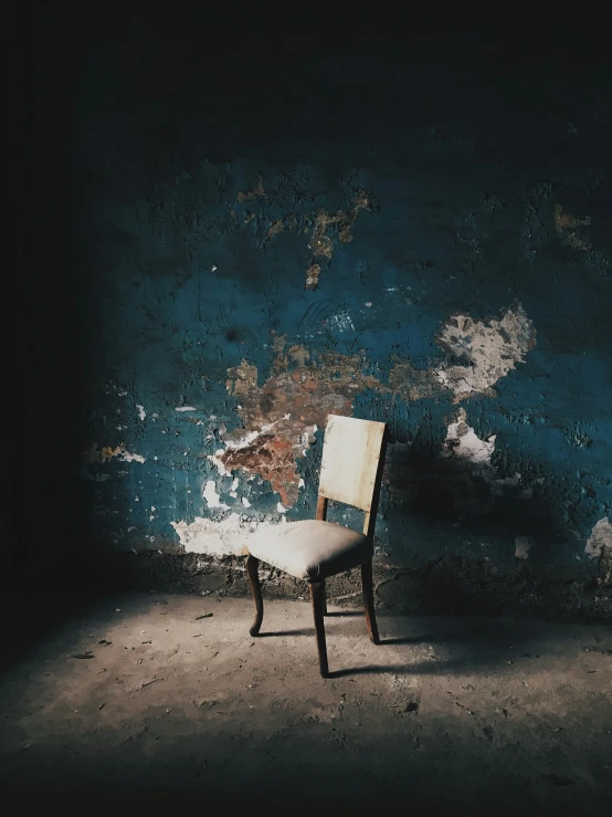 an empty chair against a dark wall with peeling paint