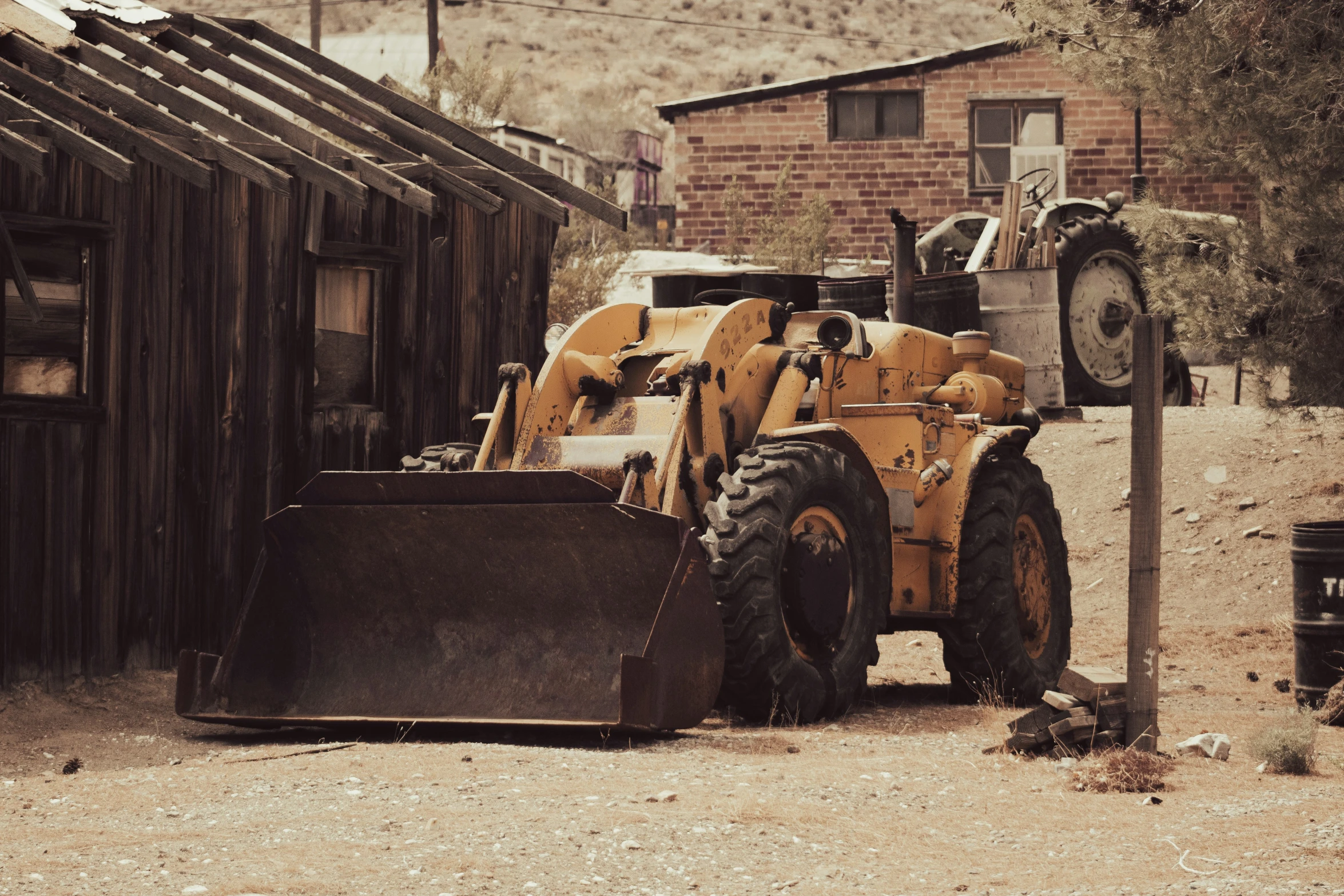 an old yellow tractor parked in a yard with the front wheel off