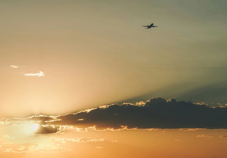 the sun setting behind a airplane flying in the air