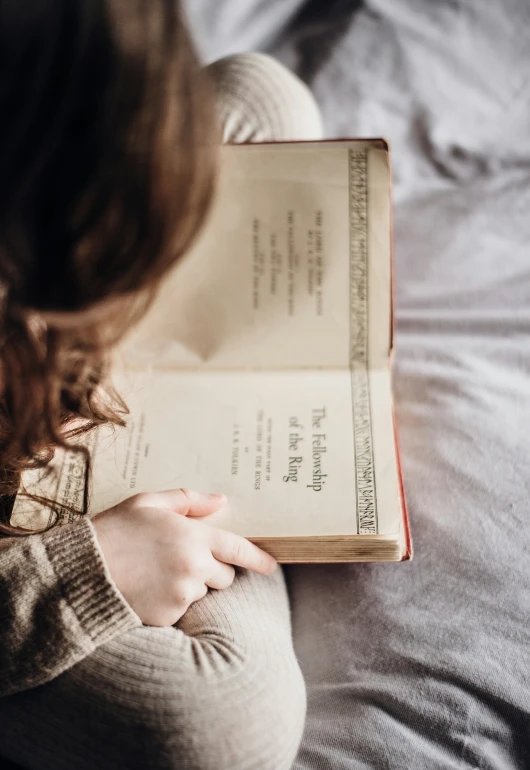 a woman is holding a book while laying in bed