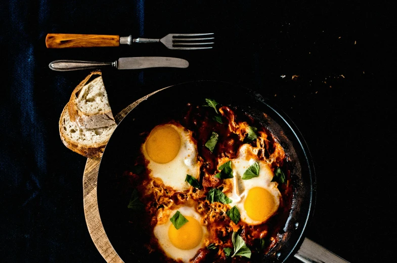 eggs in a pan, and bread on a black counter