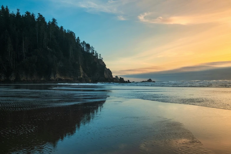 the ocean water at a beach with a small forested hillside in the distance