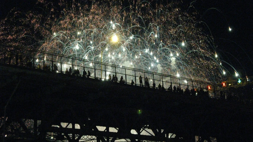 fireworks are being used over a bridge to light up the night sky