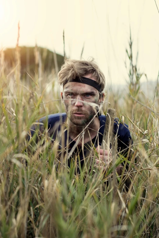 a young man is sitting in the grass looking straight ahead