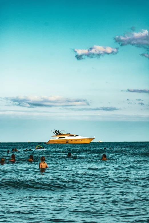 a group of people swim on the water in front of a yacht