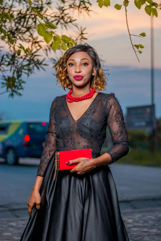 a woman standing by a tree wearing a black dress and red necktie