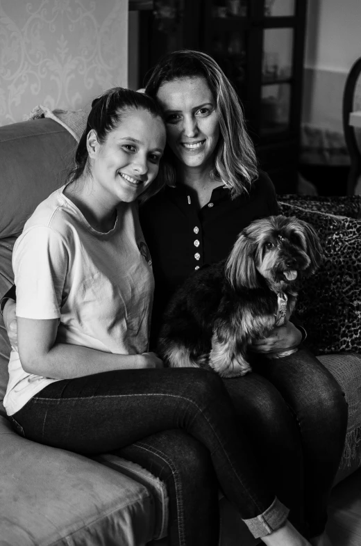 two women sitting next to a dog on a couch