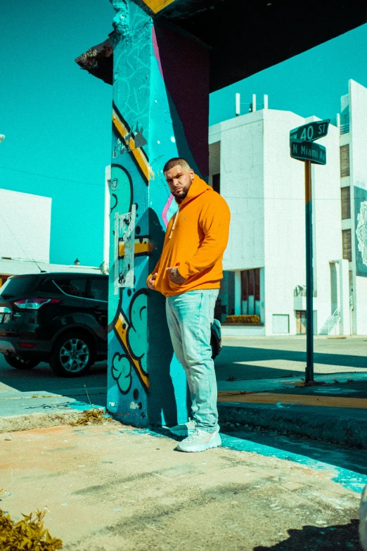 a man in an orange sweater leans against a post