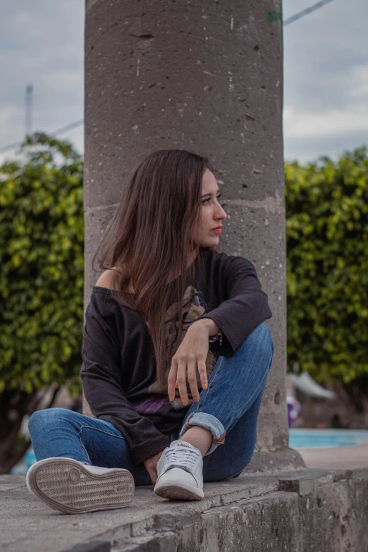 the woman sits near a building in a sweater and sneakers