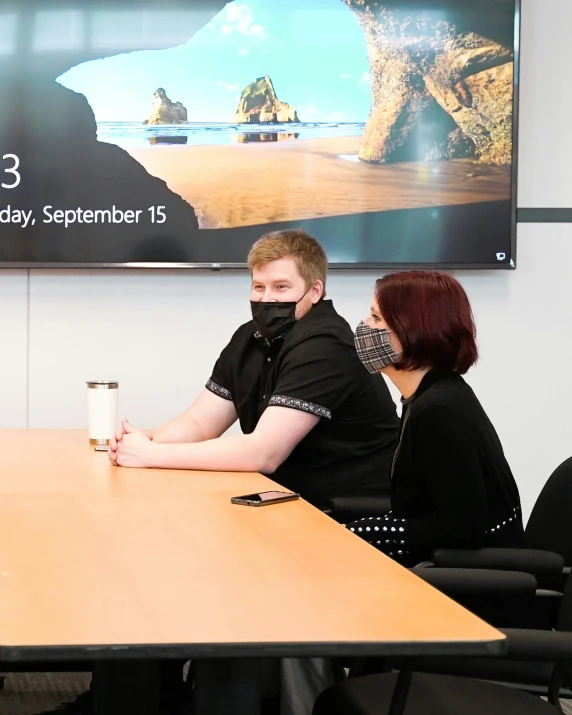 four people sitting at a desk in front of a large screen