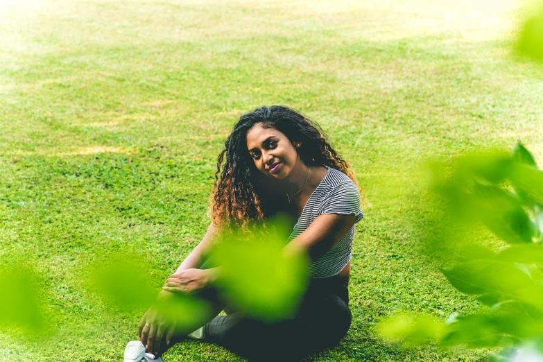 the woman is sitting on the grass near green plants