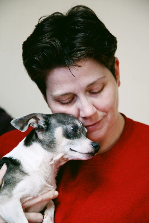 the woman smiles as she holds her small dog