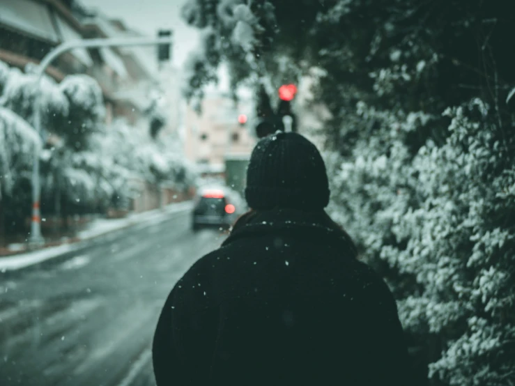 a man with his back to the camera, standing near a snowy street