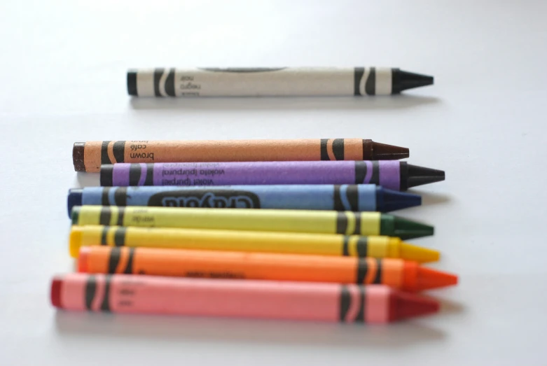 several colors of crayons, on a table, next to a crayon pencil