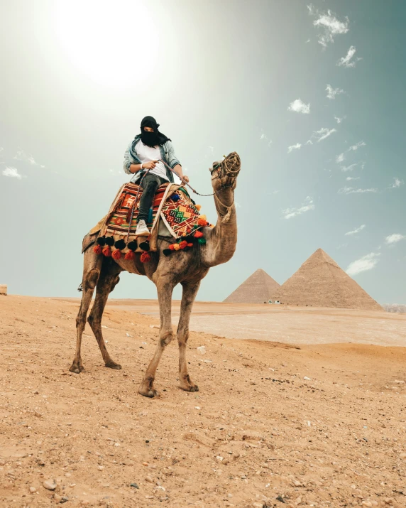 a man riding on the back of a camel in front of the pyramids