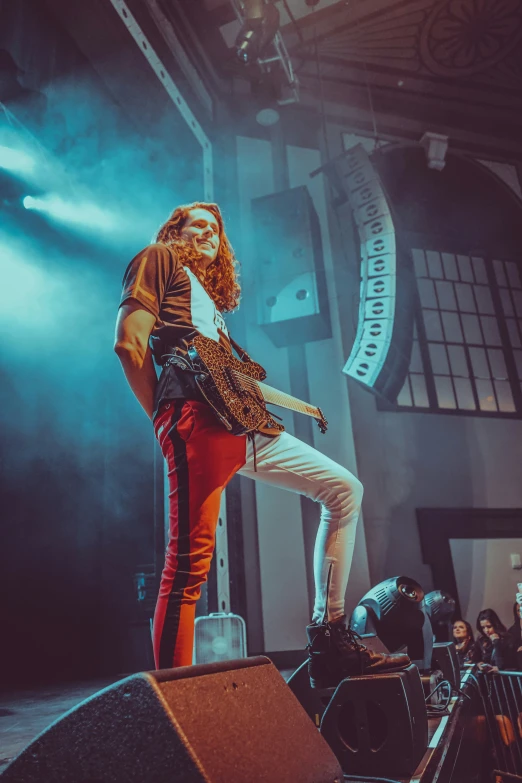 an image of a man with long red hair wearing orange pants on stage