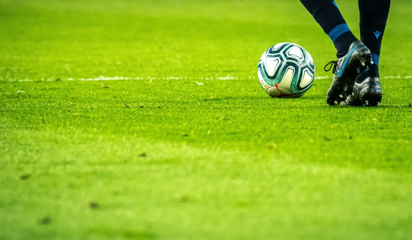 soccer ball in front of black feet, on green field