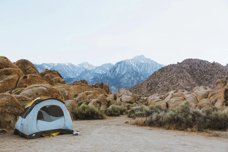 a blue and gray tent sits near a mountain range