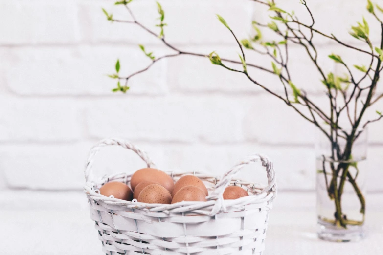 a white basket of eggs sitting next to a vase with twigs in it
