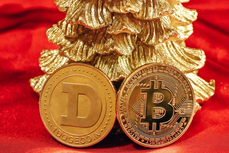 a bitcoin is sitting beside two golden christmas trees