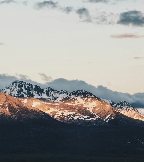 two mountain peaks covered in snow under a cloudy sky