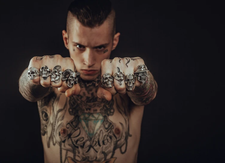 a tattooed man holds out his hands while looking at the camera
