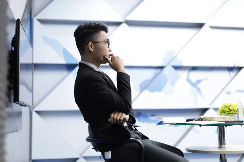 a man in a black suit sitting at a glass table