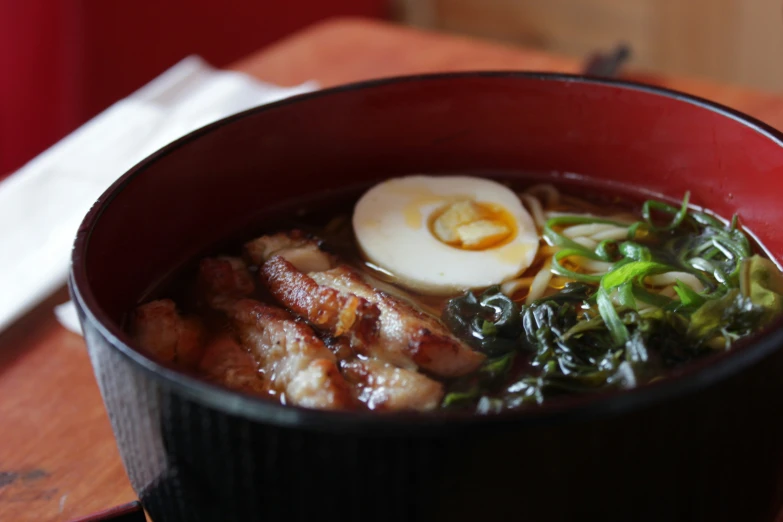 a bowl filled with noodles, greens, and a hard boiled egg