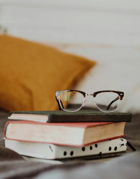 two books on a bed with glasses resting on each one